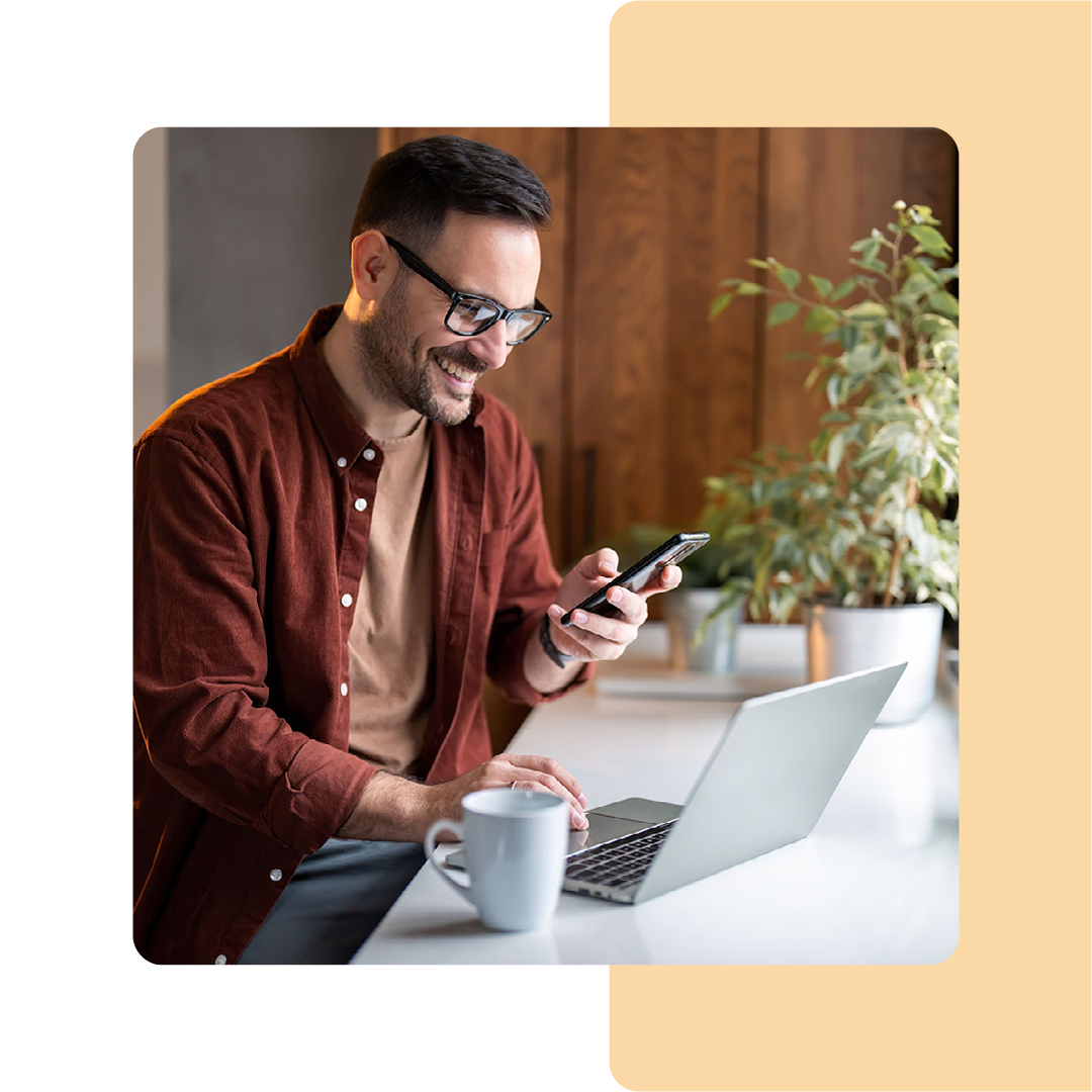 Image of a person working on a laptop and holding a mobile phone