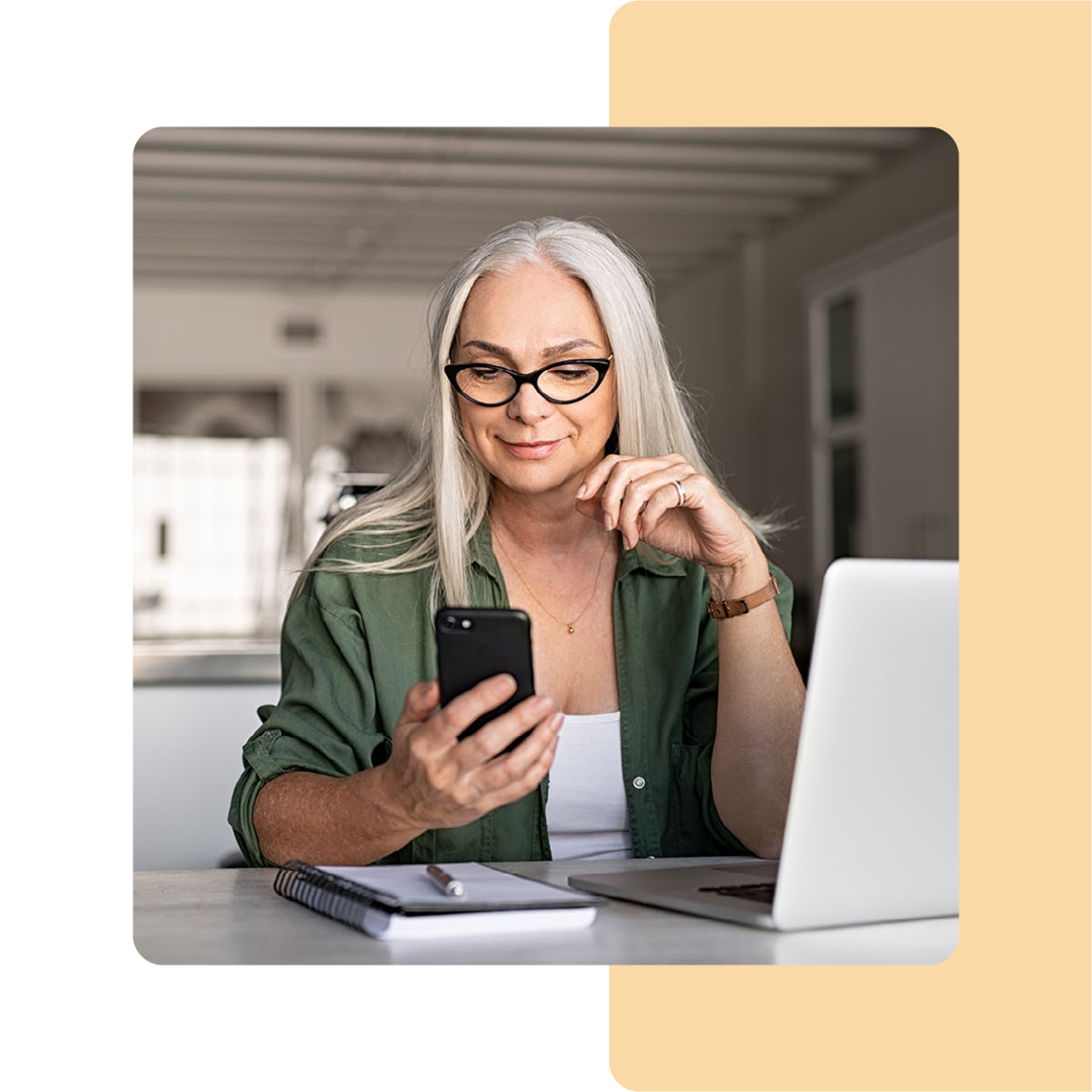 Image of a person holding a mobile phone while working on a laptop