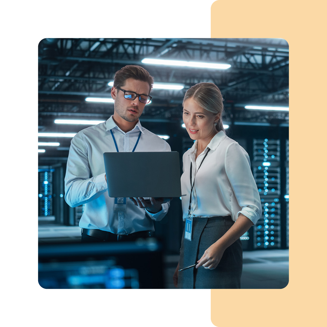 Image of two IT professionals stood in a server room holding a laptop