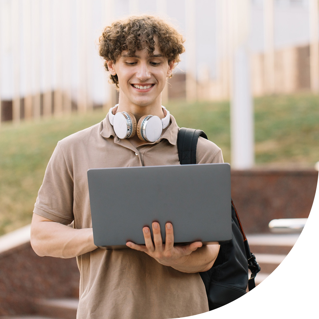 Image of a smiling university student stood on campus holding a laptop