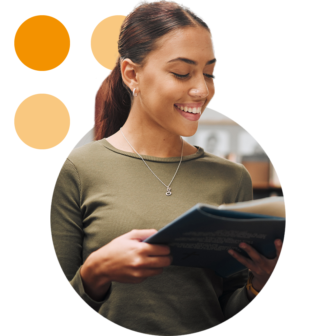 Image of a smiling university student stood in a library reading a book